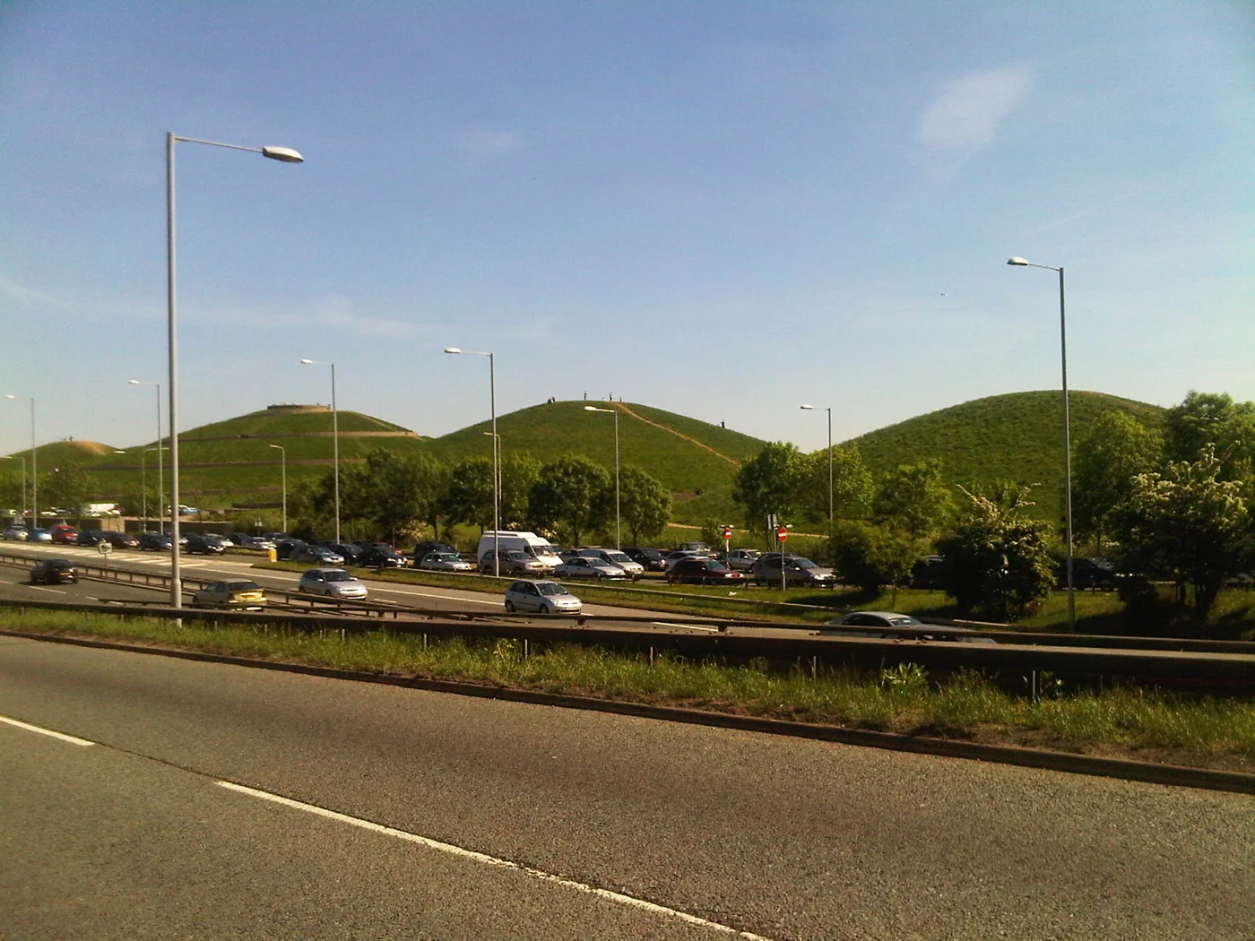 The grass mounds of Northala Fields in Northolt seen from the A40, with a path curving round the base